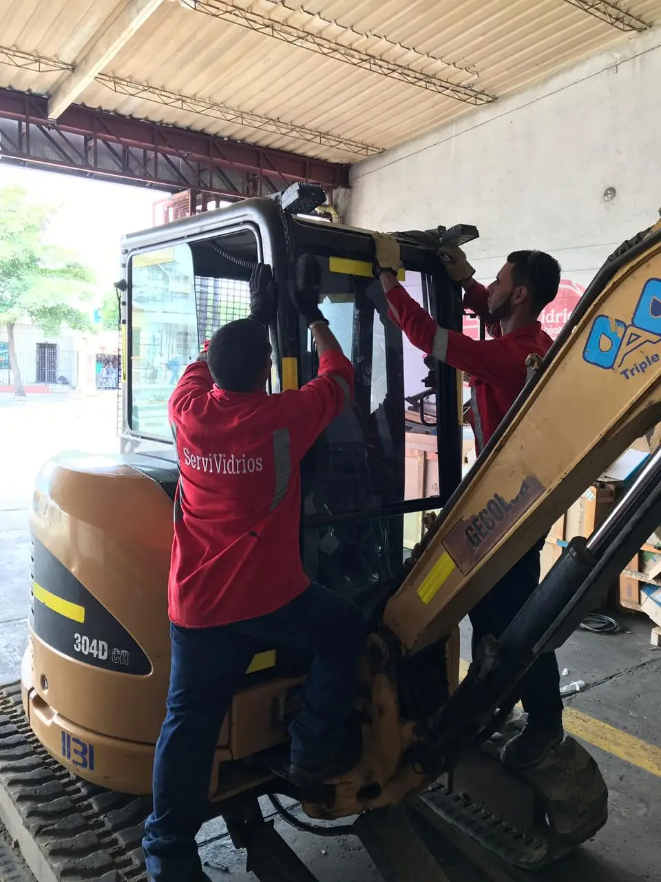 Técnicos de Servividrios instalando el vidrio de la cabina de una retroexcavadora